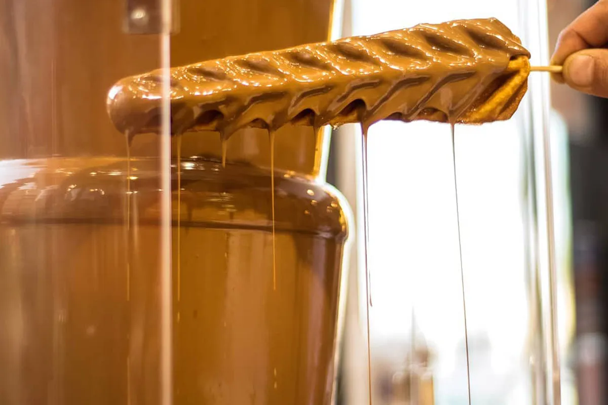 A Lotus skewer dipped into a flowing chocolate fountain